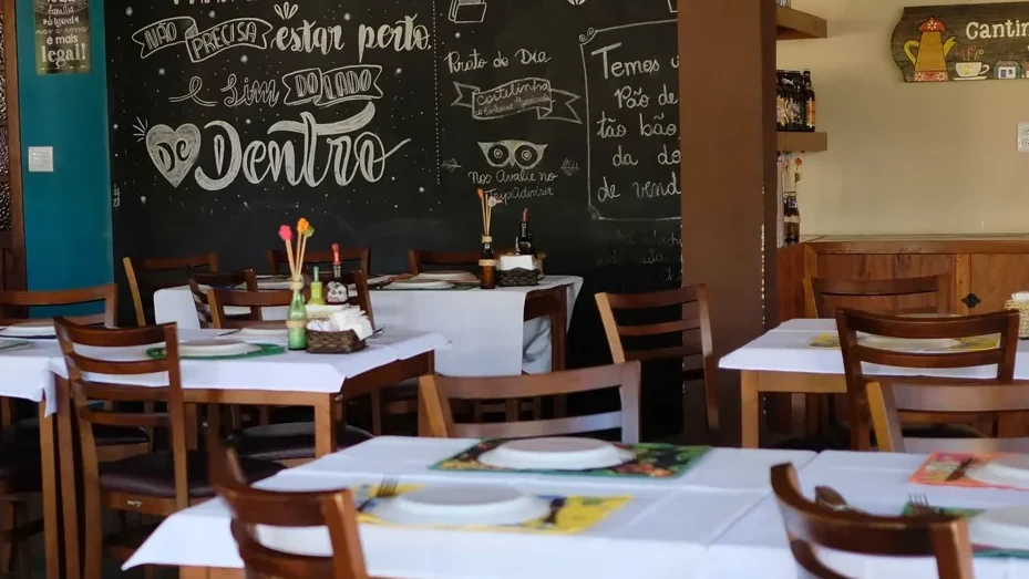 Salão do Restaurante do Chico com mesas de toalha branca, cadeiras de madeira e quadro-negro pintado à mão, onde se serve comida mineira em São Lourenço.